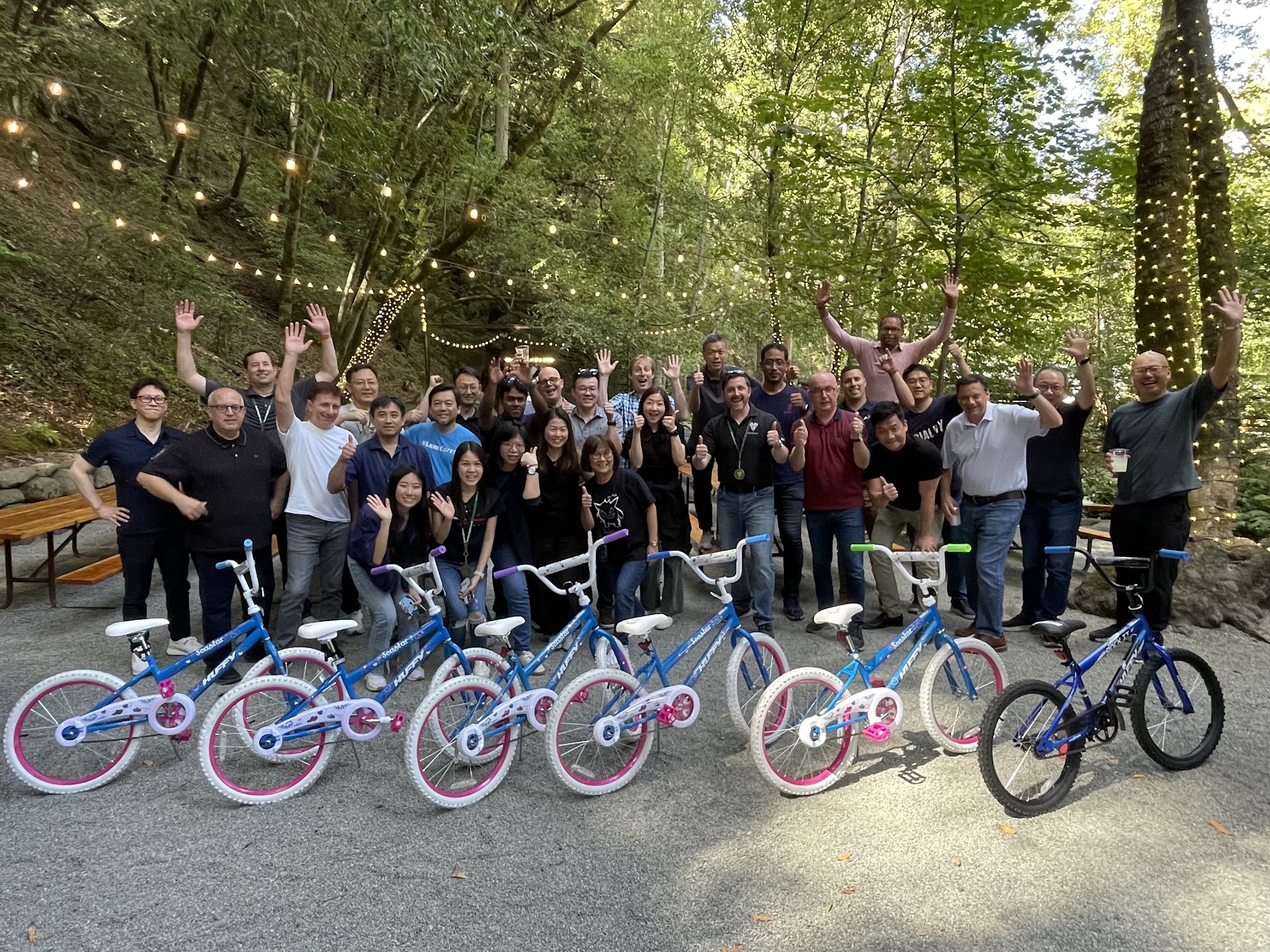 A team celebrating with the bicycles they built at Saratoga Springs, beneath trees and string lights