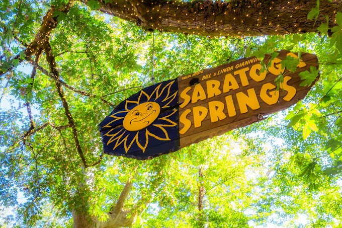 The Saratoga Springs welcome sign hanging among leafy trees